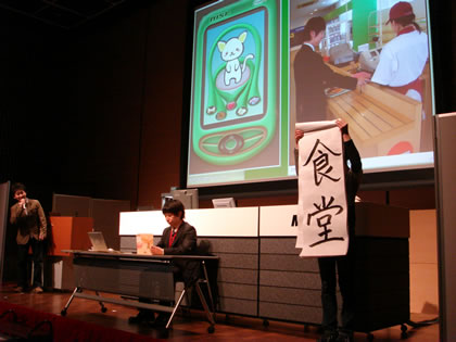 　マイクロソフトが全世界の学生を対象に開催する技術コンテスト「Imagine Cup 2006」の日本代表チームを決める選考会「The Student Day 2006」が、3月31日に東京千代田区の秋葉原コンベンションホールで開催された。Imagine Cupは2003年から開催されており、今年で4回目。世界170カ国、5万人以上（速報値）の高校生、大学生が予選に挑む大規模な大会となっている。Imagine Cupには、専門分野の異なる8つの部門があるが、その中でも特にアプリケーション開発にフォーカスした「ソフトウェアデザイン部門」の日本代表を決める最終選考会が行われた。代表の座を掛けて、日本大会での入選上位3チームがプレゼンテーションに臨む。
