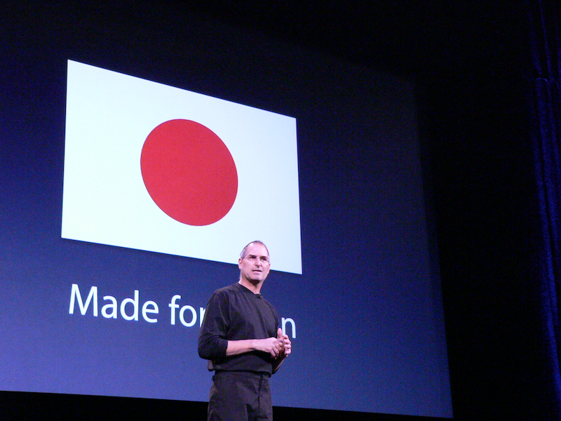 2005年8月4日に行われたiTunes Music Storeの日本でのサービス開始の会見で、日本の国旗をスクリーンに映しながら説明するスティーブ・ジョブズ