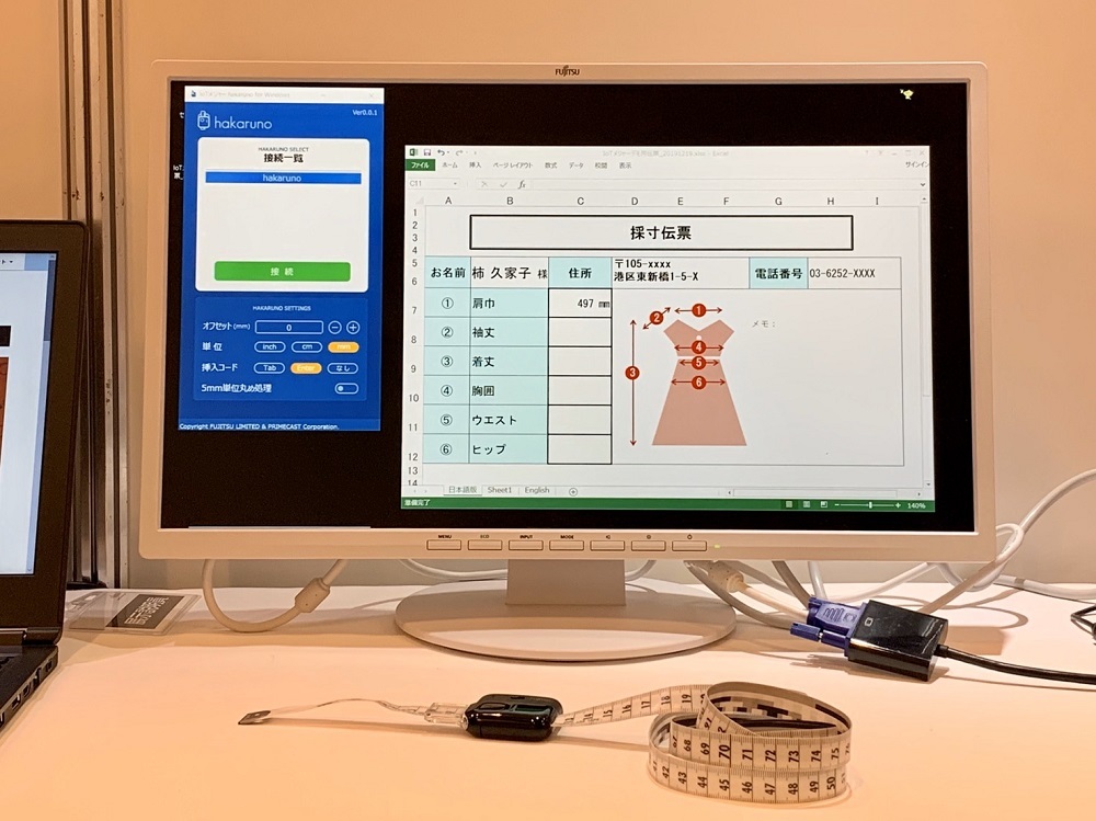 hakarunoアプリ（画面左）と採寸結果（画面右）。中央手前にあるのがIoTメジャー hakaruno。メジャーでは採寸している箇所までは認識しないため、作業従事者は採寸する項目と順番を事前に決めておき、その通りに測る必要がある