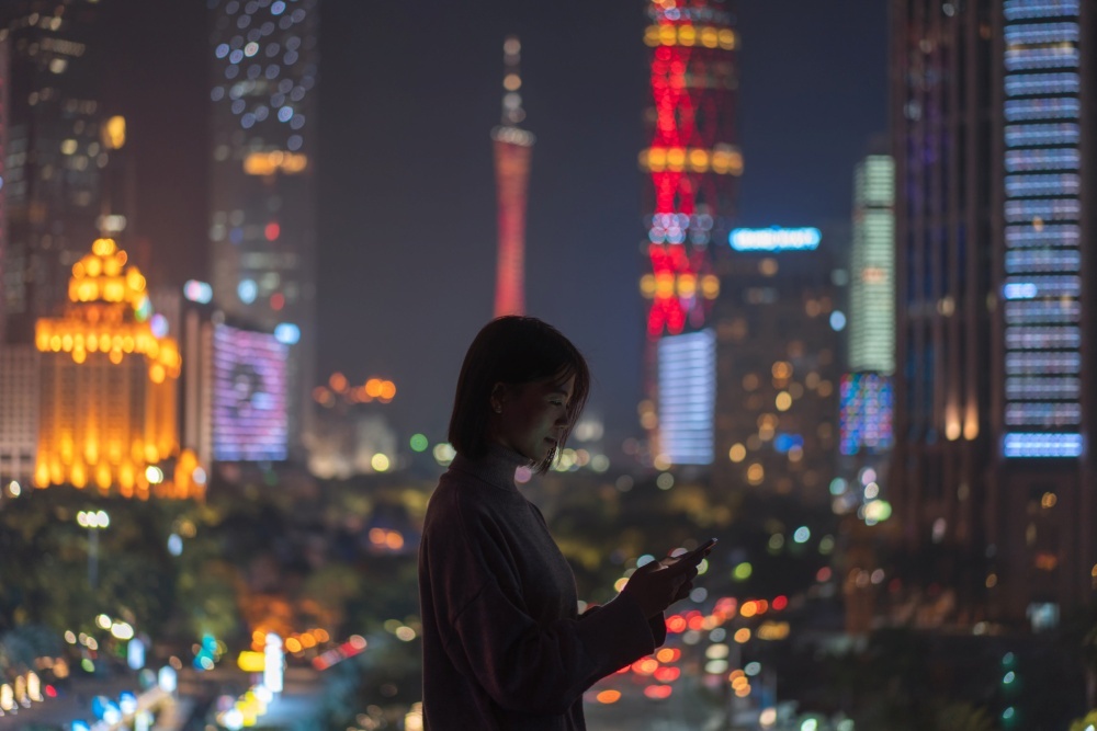 都会の夜景を背景にスマートフォンを持つ人